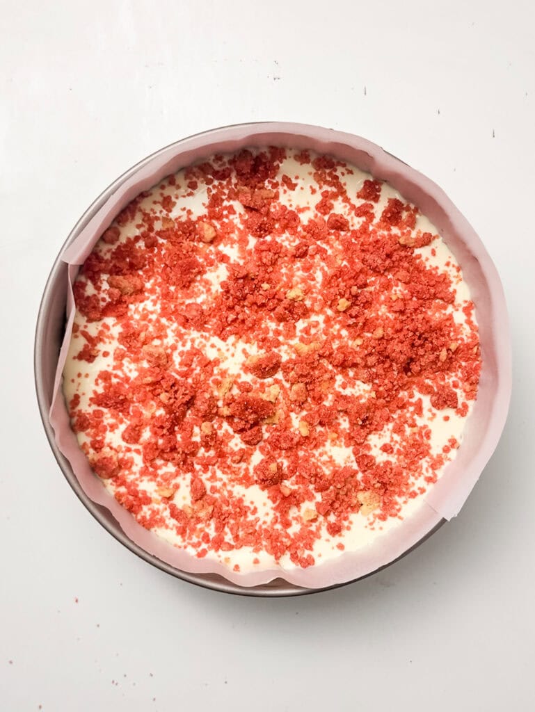 putting strawberry crunch topping in the strawberry crunch cheesecake