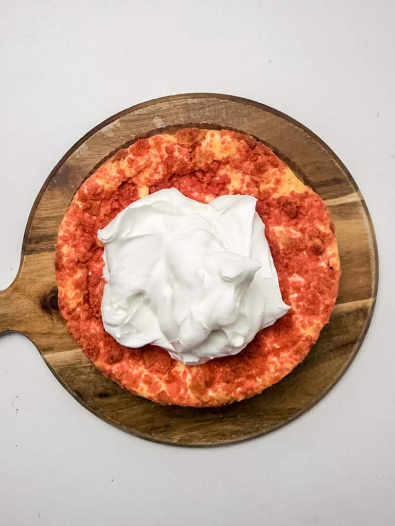 adding whipped cream ontop of strawberry crunch cheesecake