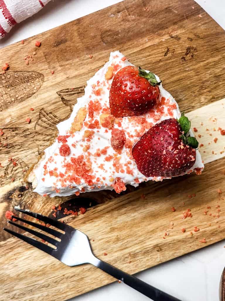 slice of strawberry crunch cheesecake on a cutting  board