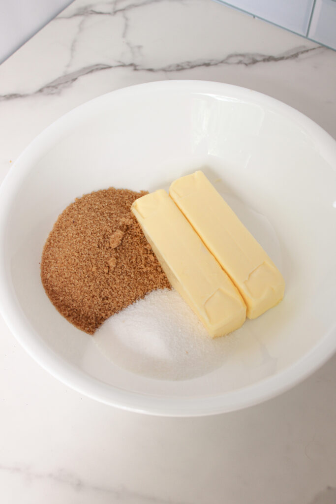 Butter, brown sugar, and granulated sugar in a white mixing bowl ready to cream.