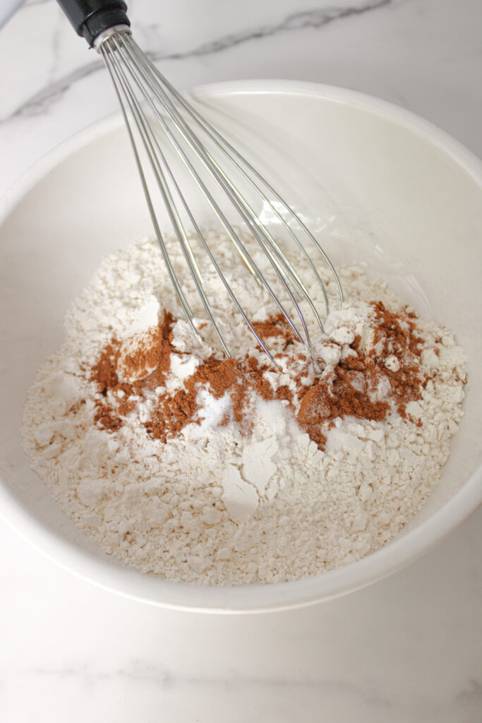 Flour, pumpkin pie spice, and salt being whisked together in a white mixing bowl.