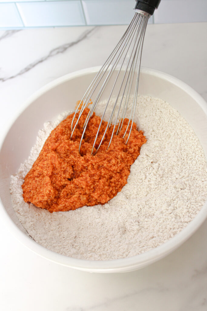Pumpkin mixture being combined with dry ingredients in a white mixing bowl.