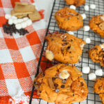 Pumpkin s’mores cookies with chocolate chips and marshmallows cooling on a wire rack.