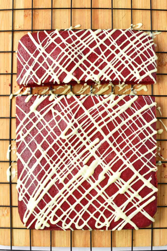 Red velvet bars drizzled with white chocolate cooling on a wire rack.