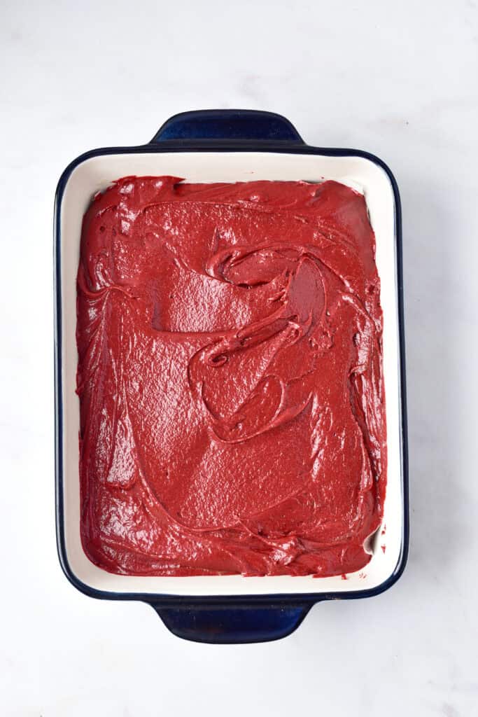 Smooth red velvet brownie batter spread evenly in a rectangular baking pan.