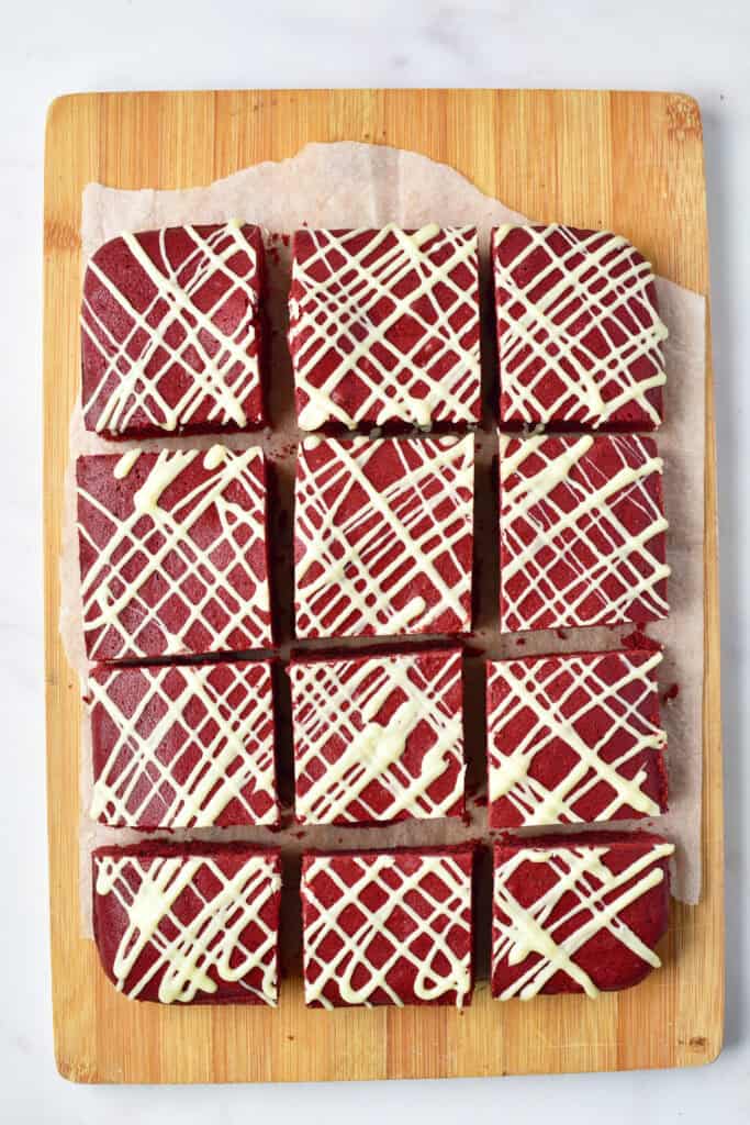 Soft red velvet brownies cut into squares and drizzled with white chocolate.