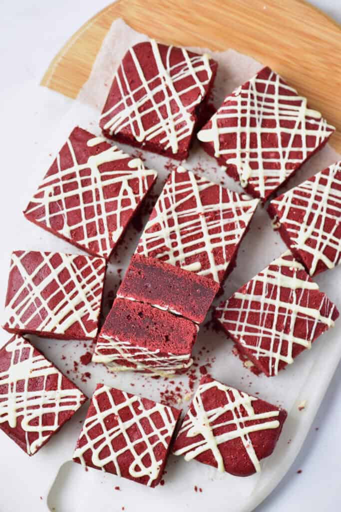 Red velvet brownies topped with white chocolate drizzle cut into neat squares.
