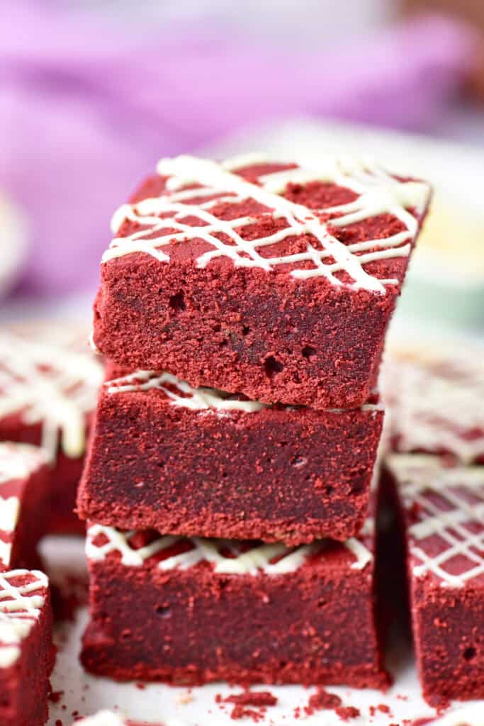 Soft red velvet cookie bars stacked and drizzled with white chocolate.
